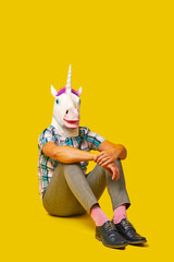 man wearing a unicorn mask sitting on the floor - obrazy, fototapety, plakaty