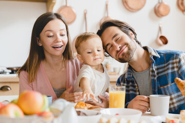 Obraz na płótnie Canvas Family dinner lunch breakfast at home. Caucasian happy parents eating together, feeding small little kid child toddler new born baby infant at home kitchen. Adoption concept