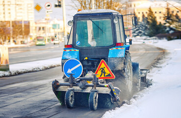 Tractor sweeping snow from sidewalk with rotating brush and removig ice and snow from road,...