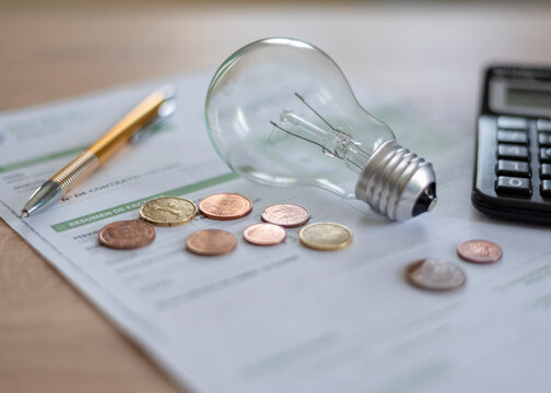 Electricity bill with light bulb, several coins, calculator and pen on the desk. Concept of electricity prices and tax payments.