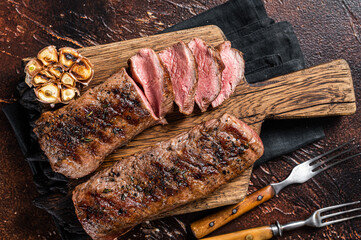 Grilled Lamb sirloin fillet meat on wooden board with herbs, mutton loin steak. Dark background....
