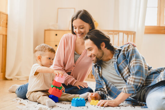 Young happy family parents playing with blocks at home with little small toddler kid child son daughter infant new born baby, developing imagination skills. Parenthood