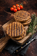 BBQ Grilled plant based meat burger patties,  vegan cutlets on wooden board with herbs. Dark background. Top view
