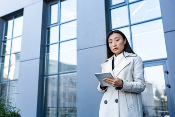 Business woman using tablet computer, office worker near office center, thoughtful and successful woman freelancer