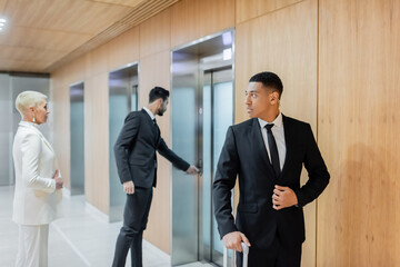 interracial bodyguards escorting senior businesswoman near elevators in hotel.