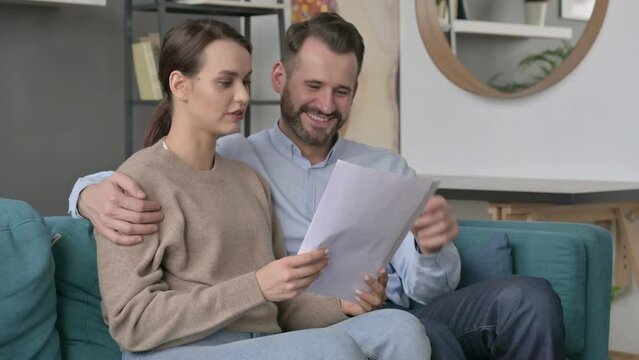 Couple Celebrating Success while Reading Documents on Sofa 