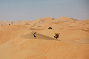 Fototapeta na wymiar Man walking on sand dune. Tourist in desert landscape. Abu Dhabi, United Arab Emirates