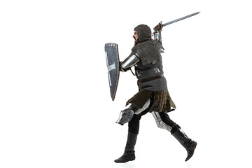 Portrait of concentrated man, medieval warrior in chain armor with sword and shield attacking enemy isolated over white studio background