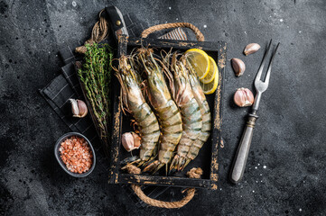 Raw fresh Giant Black tiger prawns shrimps in a tray with lemon and thyme. Black background. Top...
