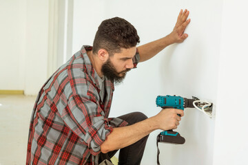 Bearded electrician fixing electricity on the wall, holding a drill to drill the wall to decorate the electrical system in the house. 