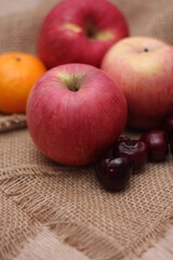 Apples and cherries are placed on a wooden table and cloth sacks.