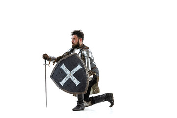 Portrait of serious manm medieval warrior, knight in special protective covering sitting on one knee isolated over white background - obrazy, fototapety, plakaty