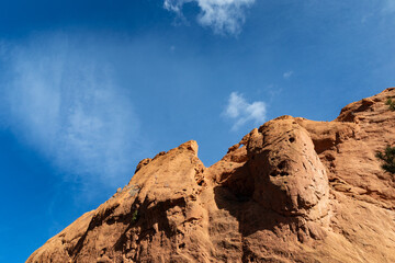 Fototapeta premium Inclined slope of brilliant orange rock ridge set against a deep blue sky with light clouds, horizontal aspect