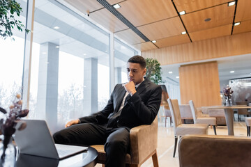 pensive african american guard sitting in hotel lounge and looking at laptop.