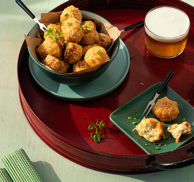 Codfish fritters server on tray with fresh herbs and glass of beer