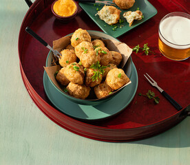 Codfish fritters server on tray with fresh herbs and glass of beer