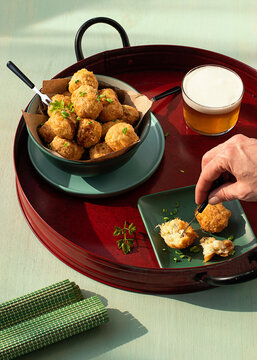 Anonymous person eating codfish fritters server on tray with fresh herbs and glass of beer