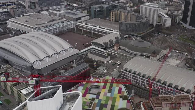 Aerial footage of colourful roof on modern building near Messe halls. Fly over tower crane on construction site. Frankfurt am Main, Germany
