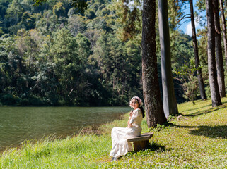 Fototapeta premium attractive Asian woman in white dress sitting in pine forest riverside at Pang Ung reservoir lake and mountain view in Mae Hong Son, Thailand
