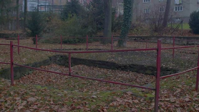 A red fence encloses a pit with autumn leaves. Place of collection and accumulation of humus. Crime scene.