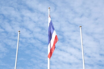 The Thai flag is on the end of the pole and 2 empty poles wite blue sky background.