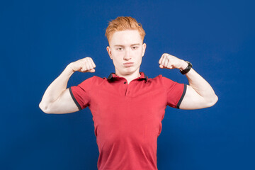Fototapeta premium A successful smiling male model happily raises her hands. Sportsman. A confident red-haired muscular man, shows muscles on his arms, is proud that he is strong and has strength