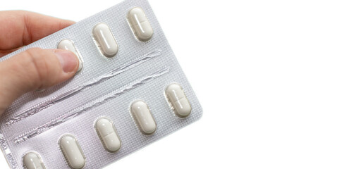 a woman's hand is removing a white pill from a plastic pack. white background and space for text. medicine and healthcare concept. 