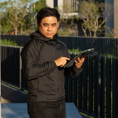 i will stalker you, asian man wear black jacket and hood look suspicious holding computer tablet do...