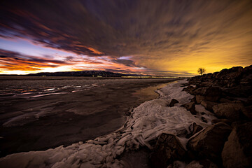 Fototapeta na wymiar Sunset and city lights glowing over Utah Lake with ice on shore