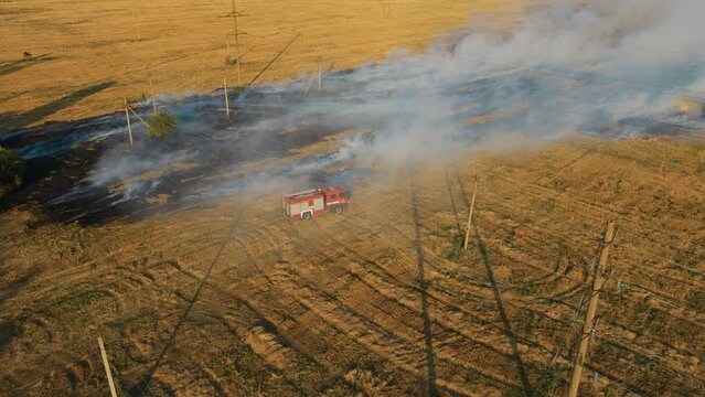Fire engine turns off flame in harvesting wheat field in smoke clouds. Emergency case for danger mission and rescue nature saving concept