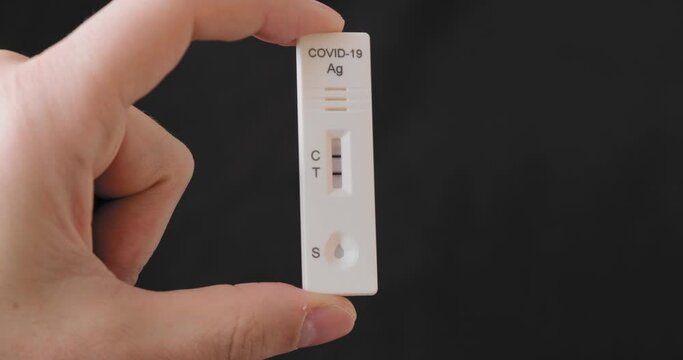Hand holds a COVID-19 Coronavirus SARS-CoV-2 positive test against black background, with both test and control strips colored. At home self test kit, rapid antigen, copy space.