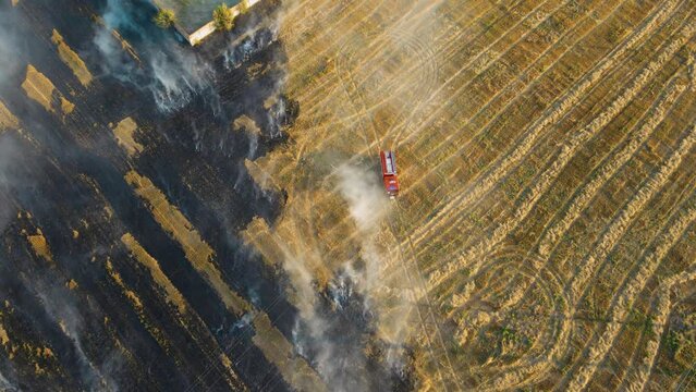 Cinematic footage brave firefighters rush to fight burning flame on agronomic field with clouds of smoke and fire truck with water driving by danger dry stubble. Emergency case for danger mission and