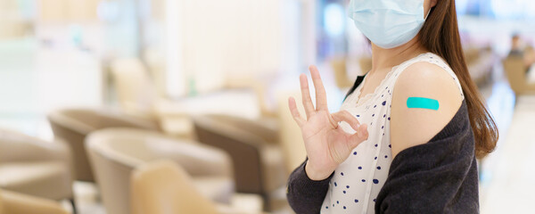 Happy Asian young woman wearing a protective face mask showing her vaccination spot on her arm.