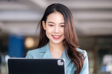 A female entrepreneur or businesswoman showing a smiling face while operating a computer tablet working on a wooden table.