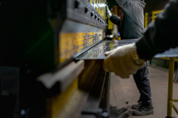 Workers handling piece of metal sheet into a folding machine	
