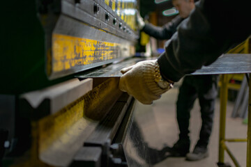 Workers handling piece of metal sheet into a folding machine	