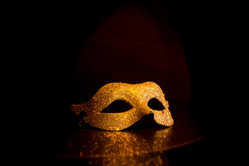 golden carnival mask under a halo of light on a black background - obrazy, fototapety, plakaty