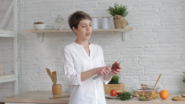A woman holding a knife and an apple takes a video tutorial on cooking, a young woman at home in the kitchen tells the recipe on camera