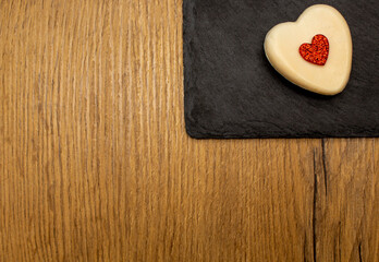 Fototapeta na wymiar Heart-shaped soap with glossy heart in the middle on black stone plate on wooden background. Love valentine concept. Flat lay