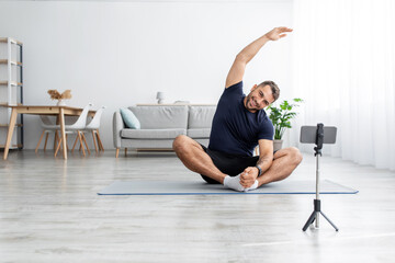 Cheerful millennial muscular caucasian guy in uniform sitting on floor on mat in lotus position, practicing yoga