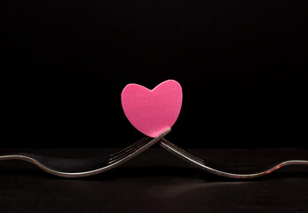 Forks with a pink heart in the middle on black background. Love valentine concept