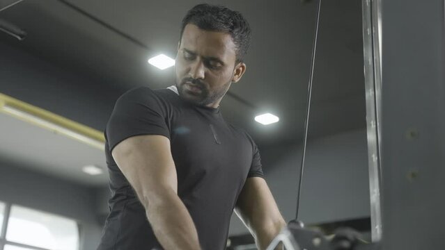 Young indian bodybuilder doing biceps workout at gym - concept of body fitness, muscle building exercise and determination.