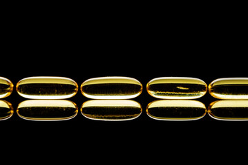 omega-3 capsules laid out in a row on a black background. Omega 3 closeup with reflection.