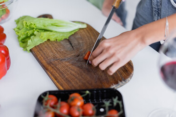 cropped view of woman cutting cherry tomato on chopping board.