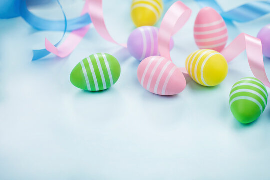 Easter eggs in pastel colors on light blue background with ribbons. Stock image with copy space