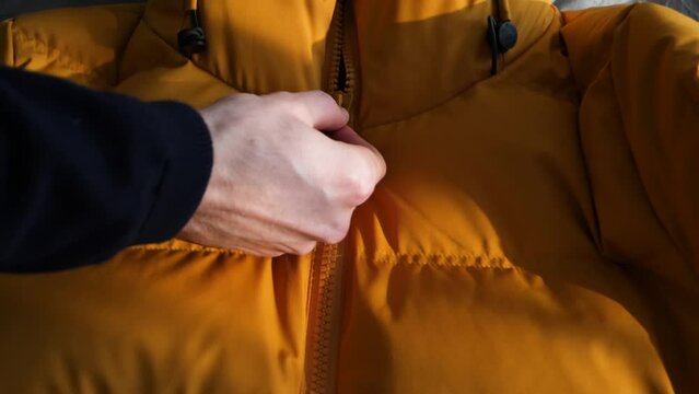 Caucasian hand opening zipper on yellow jacket in slow motion, following shot