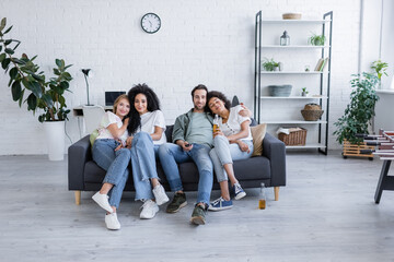 cheerful lesbian and heterosexual couples watching movie on sofa.