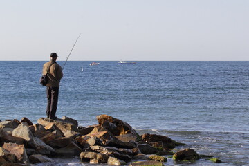 Fototapeta na wymiar fishing a fisherman stands on the rocks with a spinning rod on the seashore