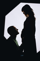 Silhouette of a stylish, smiling bearded man and a beautiful pregnant girl with a big belly on a white background in the studio.