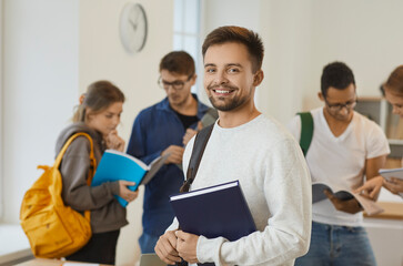 Portrait of smiling millennial Caucasian guy student with backpack pose in public or private college or university. Happy young male learner with textbooks with groupmates in school. Education.